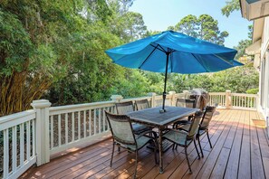A wooden deck with a table and chairs, surrounded by a white railing, and a blue umbrella providing shade. - 17 Cartgate - Palmetto Dunes - 4 Bed 4 Bath Private Pool -Hilton Head Rentals (Hilton Head Island)