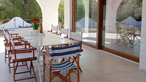 An outdoor dining area with a long table and chairs, large glass doors, and a view of greenery. - Detached villa within walking distance of Foxi and Murdegu beach (Foxi Murdegu)
