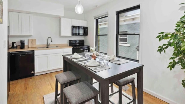 Een moderne keuken met witte kasten, een zwarte vaatwasser en een eethoek met een donker houten tafel en grijze stoelen.