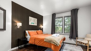 Een moderne slaapkamer met een groot bed, een nachtkastje, een stoel en een raam met gordijnen.