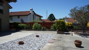Un patio con zona de estar, un edificio blanco de techo rojo y una estructura metálica alta al fondo.