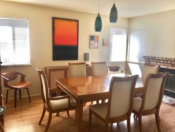 Une salle à manger avec une table et des chaises en bois, un tableau au mur et des luminaires suspendus.