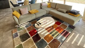 Un salon moderne avec un grand canapé d’angle, une table basse et un tapis aux couleurs vives.
