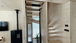 Un intérieur moderne avec un escalier en bois, une cheminée noire et un téléviseur fixé au mur.