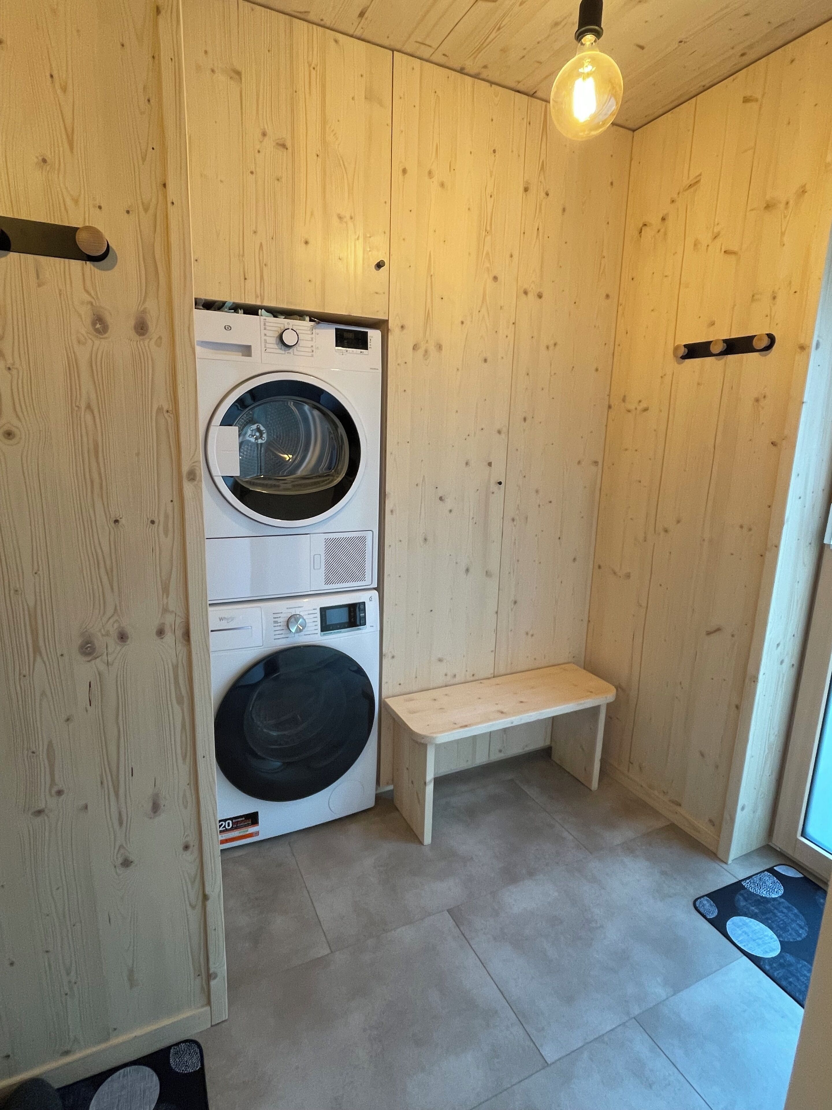 Un cuarto de lavandería con paredes de madera, una lavadora, una secadora y un banco.
