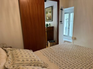 Une chambre à coucher avec un lit, une armoire en bois, un petit meuble et une fenêtre.