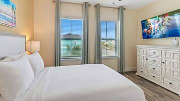 Une chambre d’hôtel avec un lit, une commode, un ventilateur de plafond et une grande fenêtre avec des rideaux.