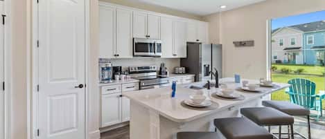 Una cocina moderna con armarios blancos, una isla central con taburetes y vistas a una zona residencial.