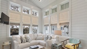 A living room with a sectional sofa, a coffee table, a wooden chair, and a TV mounted on the wall. - Home Across from Beach Access w/ Pool (Santa Rosa Beach)