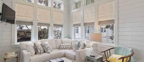 A living room with a sectional sofa, a coffee table, a wooden chair, and a TV mounted on the wall.