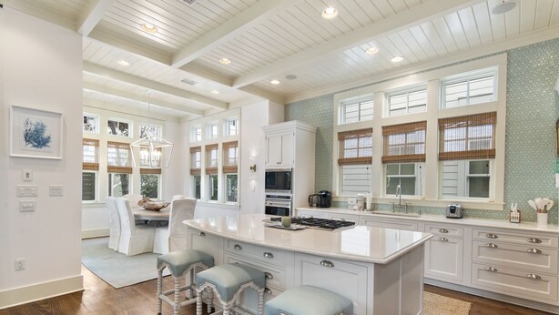 A spacious kitchen with a large island, white cabinetry, and a view of the outdoors through large windows. - Home Across from Beach Access w/ Pool (Santa Rosa Beach)