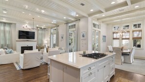 A spacious living room with a fireplace, white furniture, and a large island with a stove. - Home Across from Beach Access w/ Pool (Santa Rosa Beach)