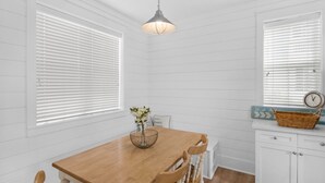 A dining area with a wooden table and chairs, white paneled walls, and a hanging light fixture. - Renovated 30A Bungalow 5 Min Walk to Beach!! (Santa Rosa Beach)