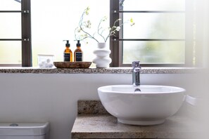 A bathroom with a white sink, a window with blinds, and two bottles of hand soap on the windowsill.