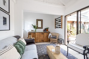 A living room with a sofa, a coffee table, a wicker chair, a small table with a lamp, a wooden cabinet, and a wine rack.