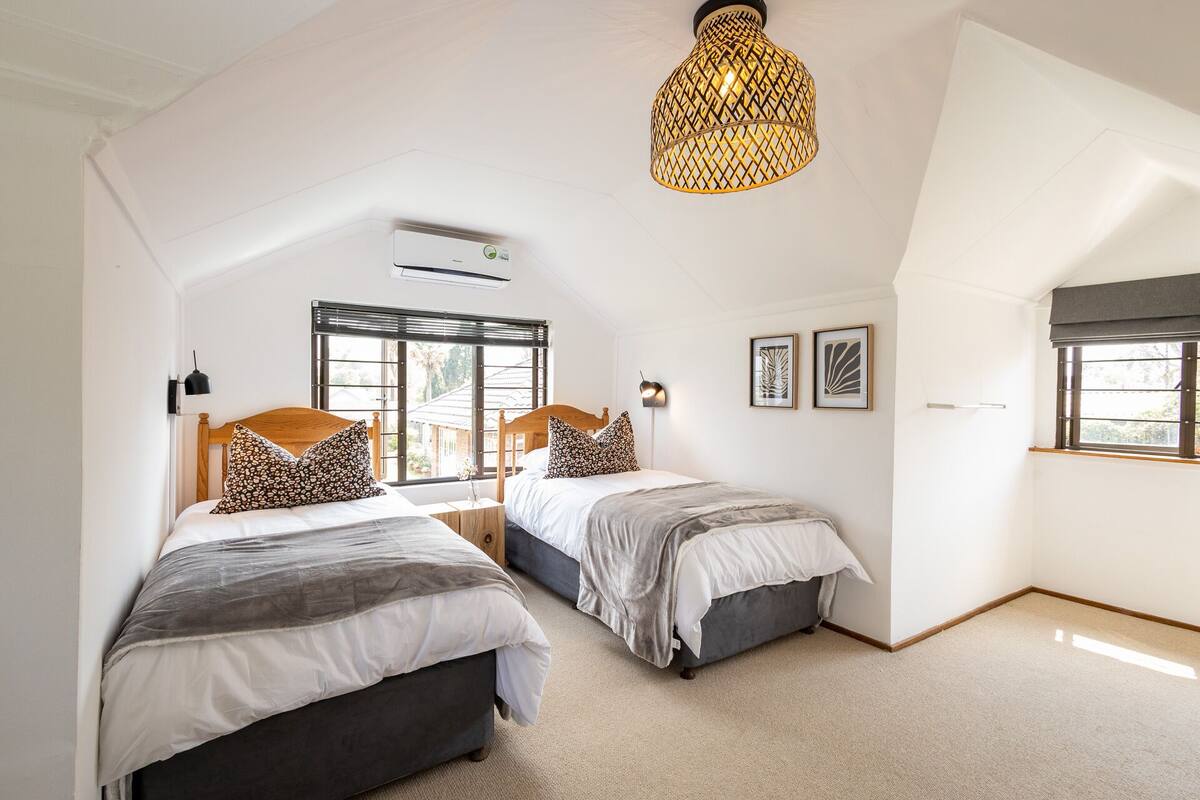 Une chambre avec deux lits, une grande fenêtre et un luminaire suspendu.