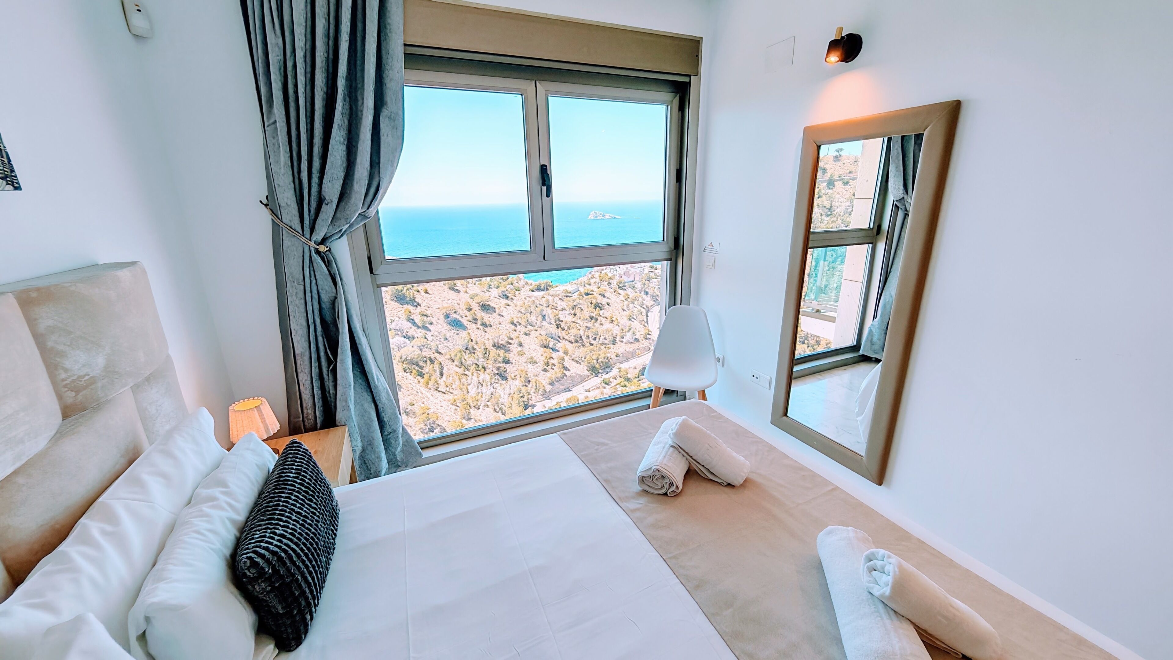 A hotel room with a large bed, a view of the landscape, a window, and a mirror.