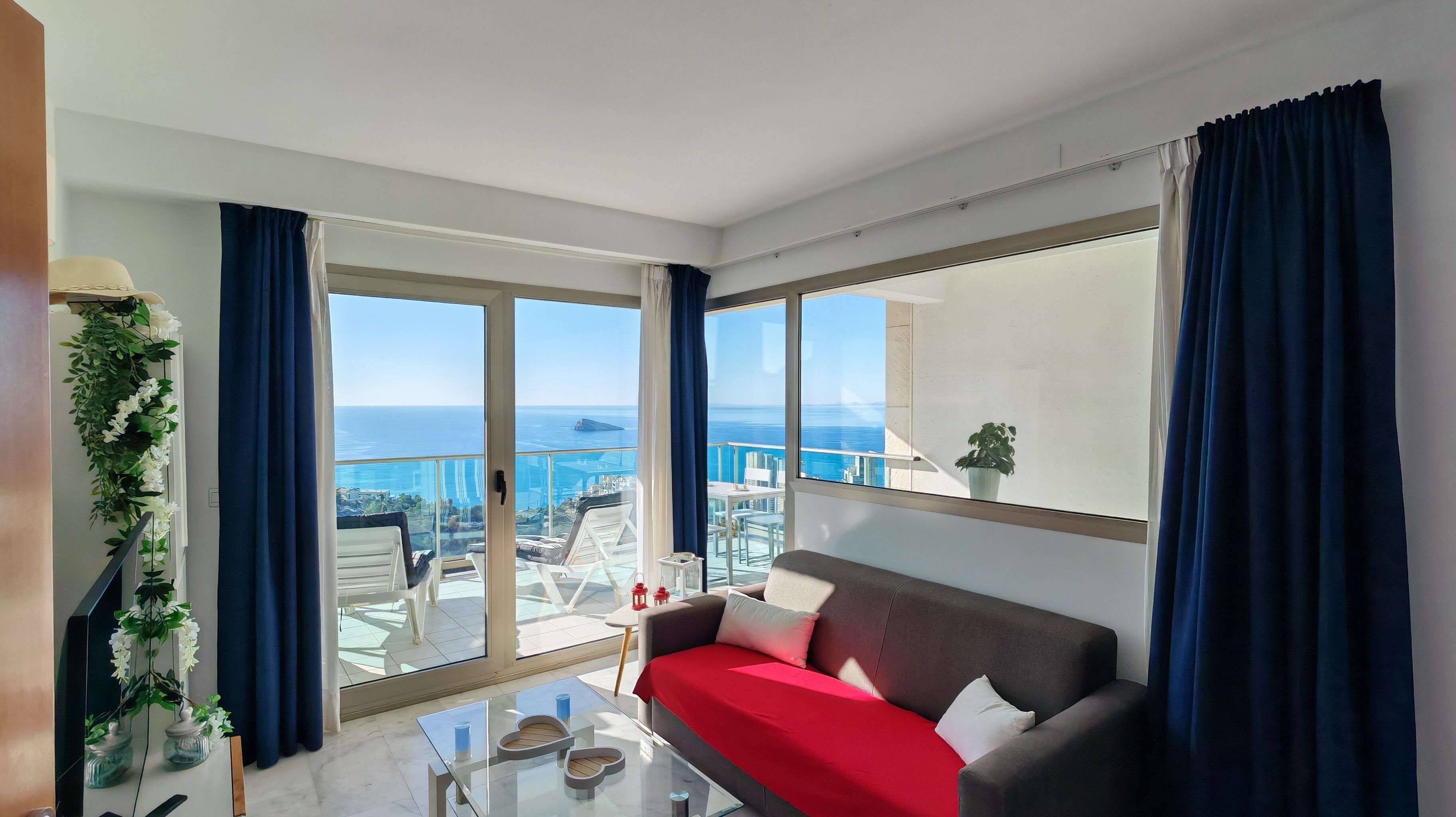 A modern living room with a sofa, a glass coffee table, and a view of the sea.