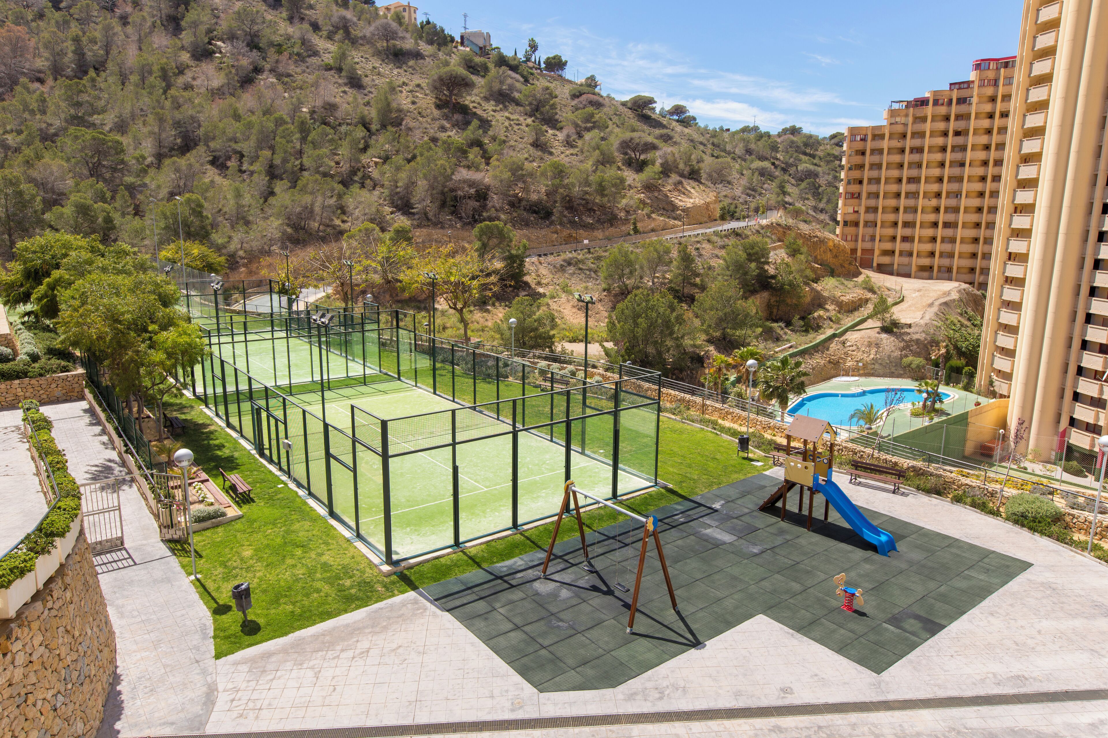 A tennis court surrounded by a fence, a playground with a slide, and a pool.