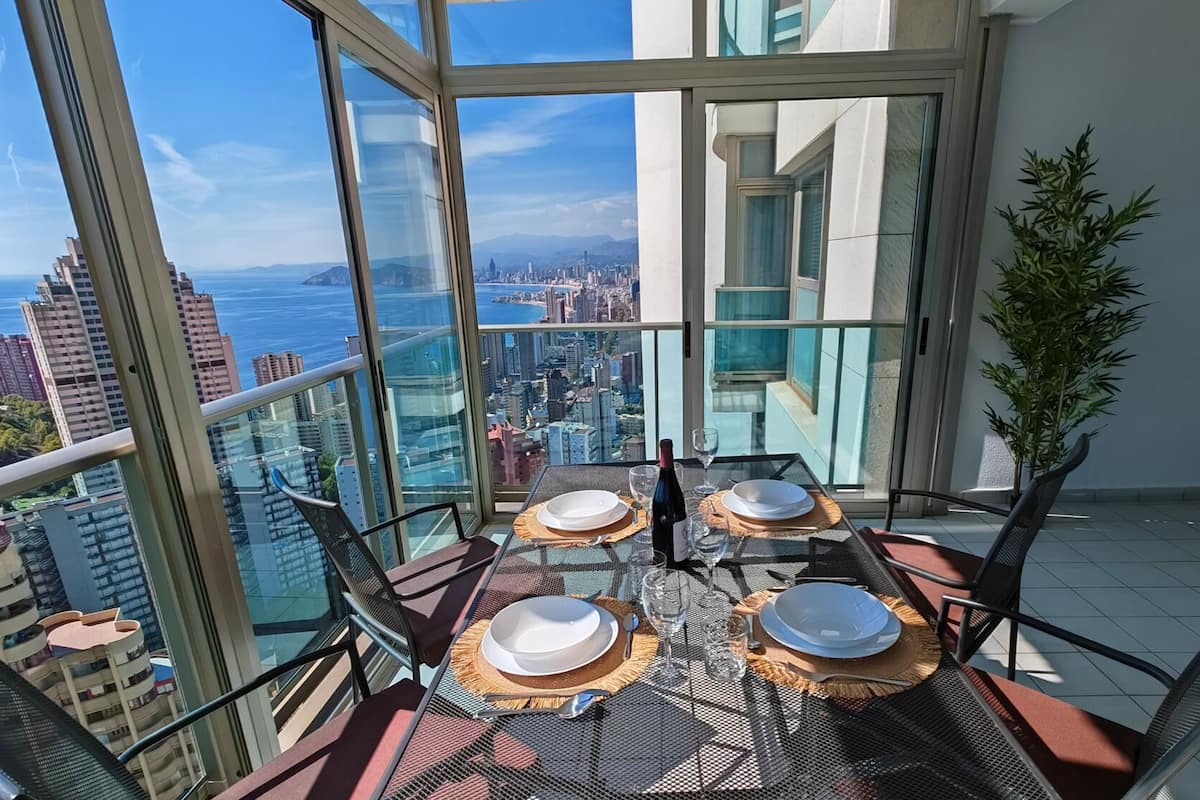 A balcony with a table set for four, overlooking a cityscape.