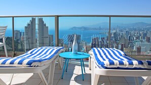 A balcony with two lounge chairs and a table, overlooking a cityscape and the sea. - Benidorm sky - High-rise apartments (Benidorm)