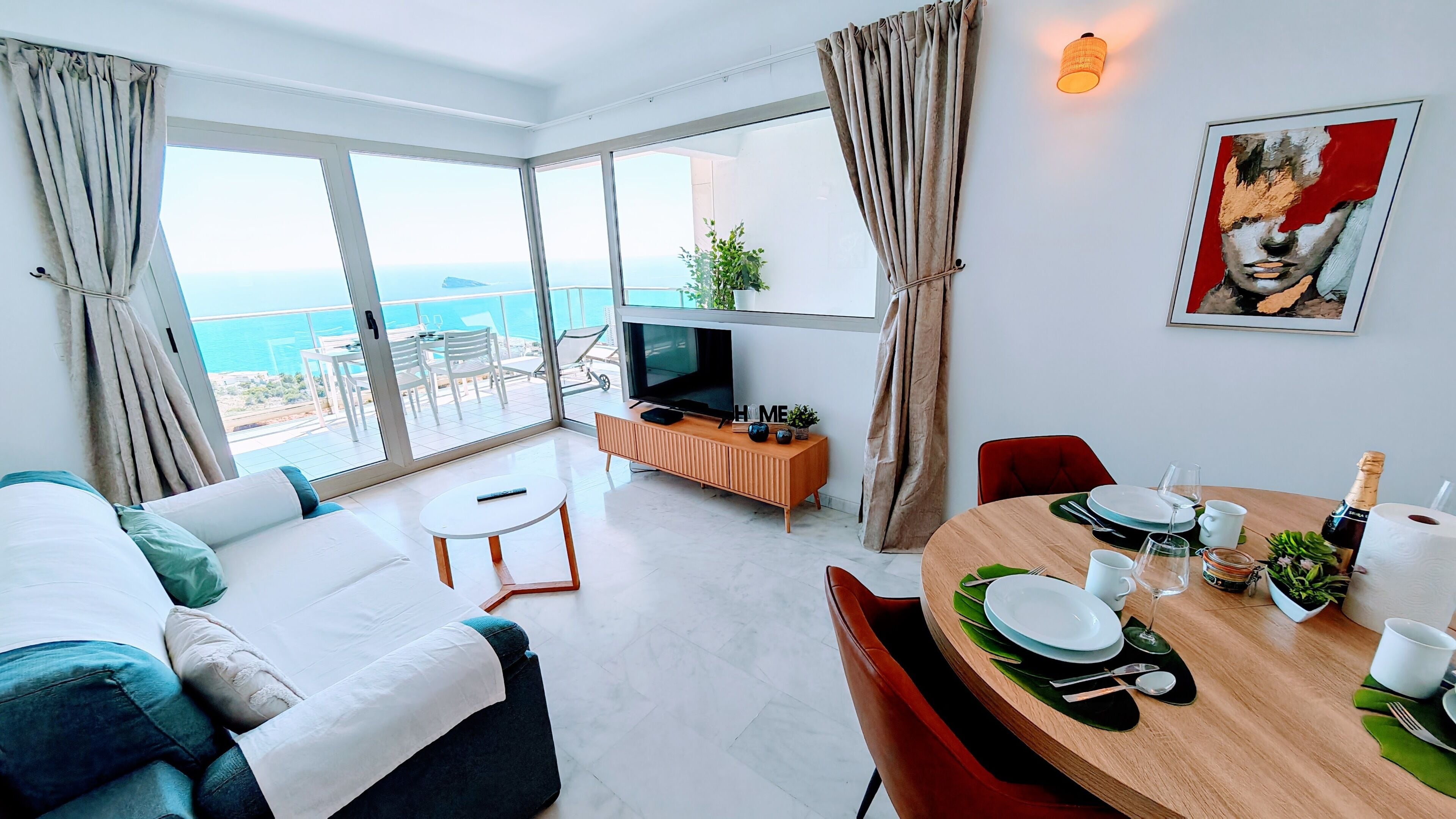 Una sala de estar moderna con televisor, sofá, mesa de comedor y un balcón con vistas.
