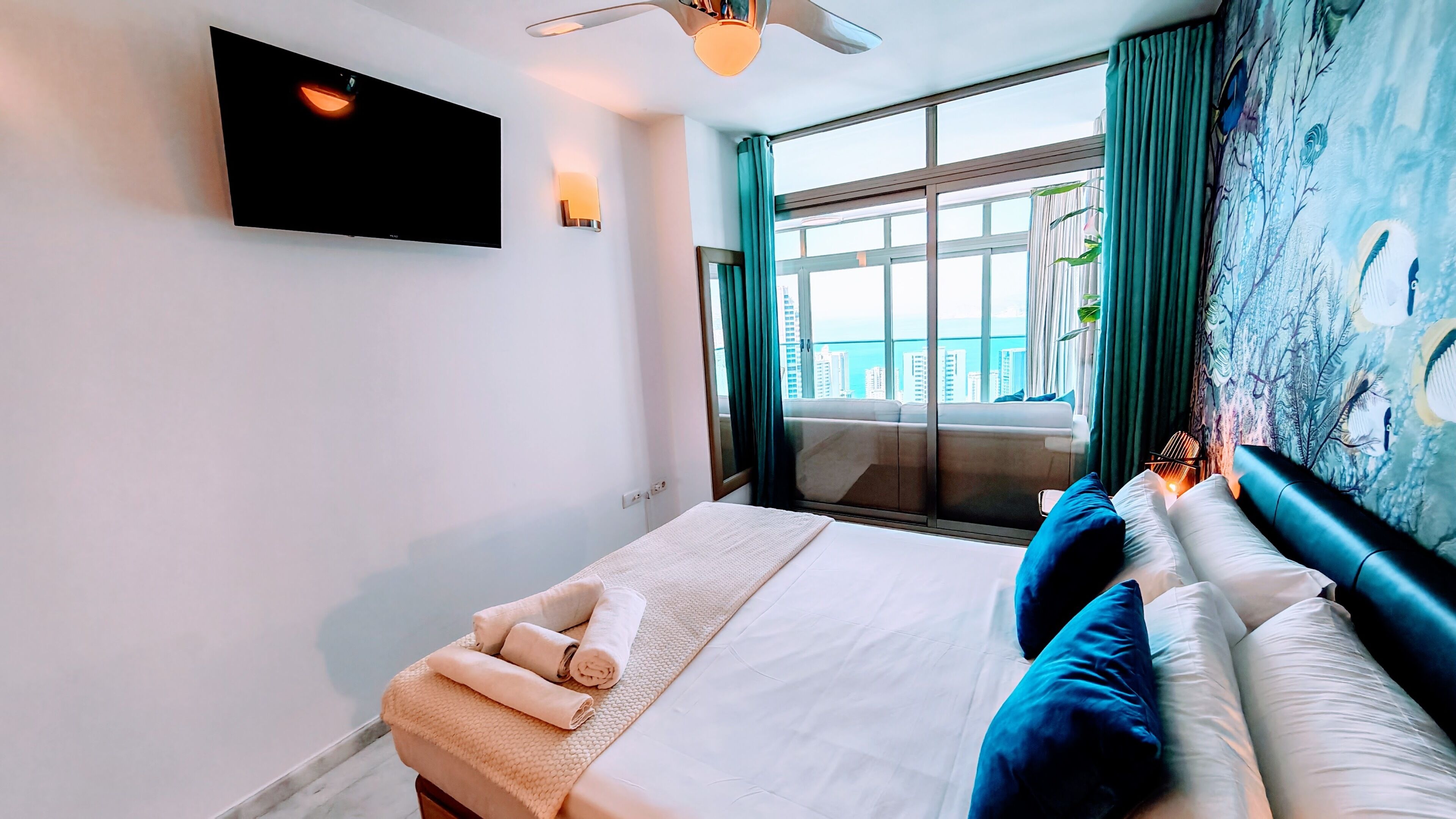 Une chambre d’hôtel avec un lit, un téléviseur à écran plat, une fenêtre avec des rideaux et une vue sur la ville.