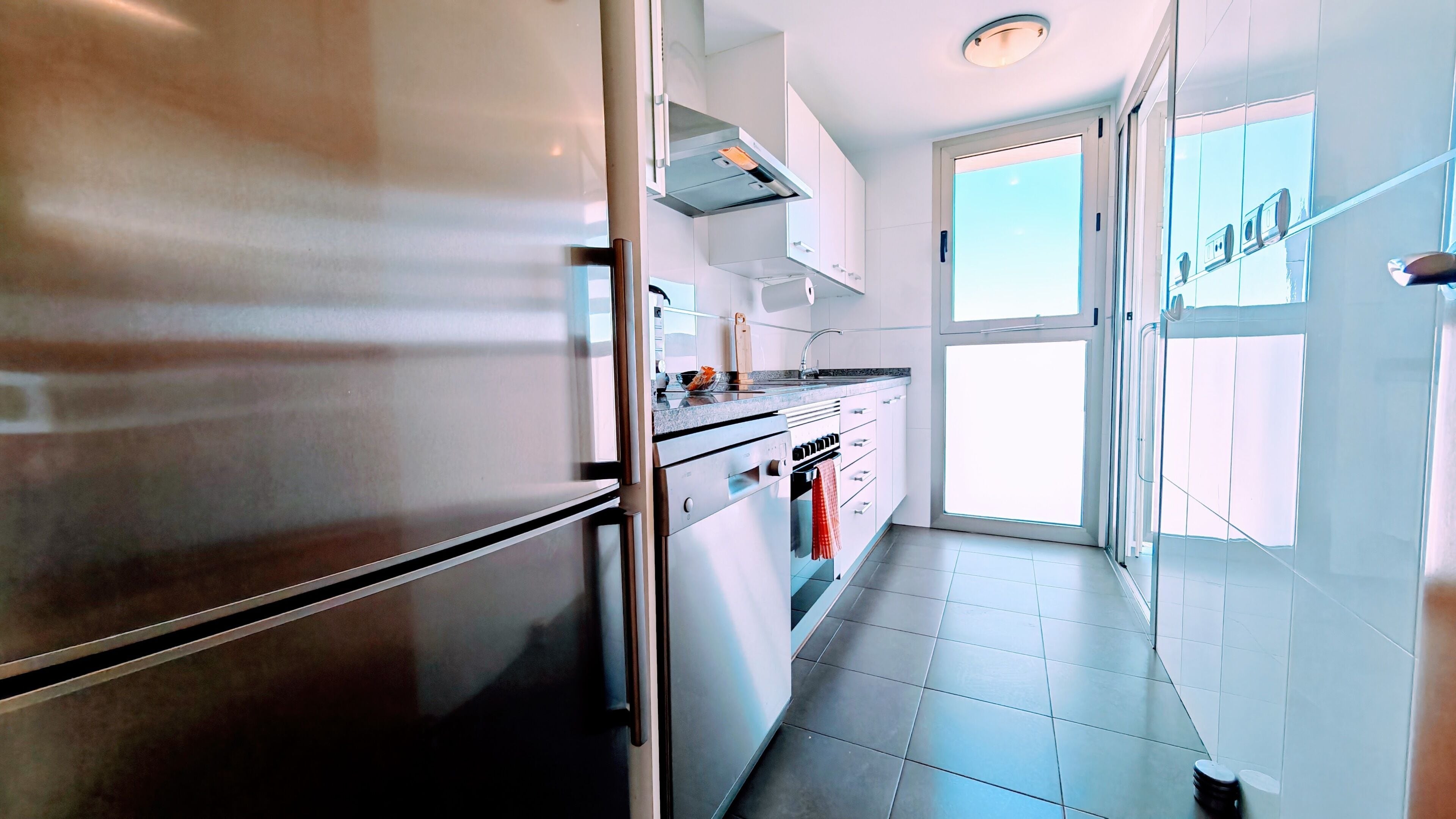 A modern kitchen with stainless steel appliances, a window, and a door leading to a balcony.
