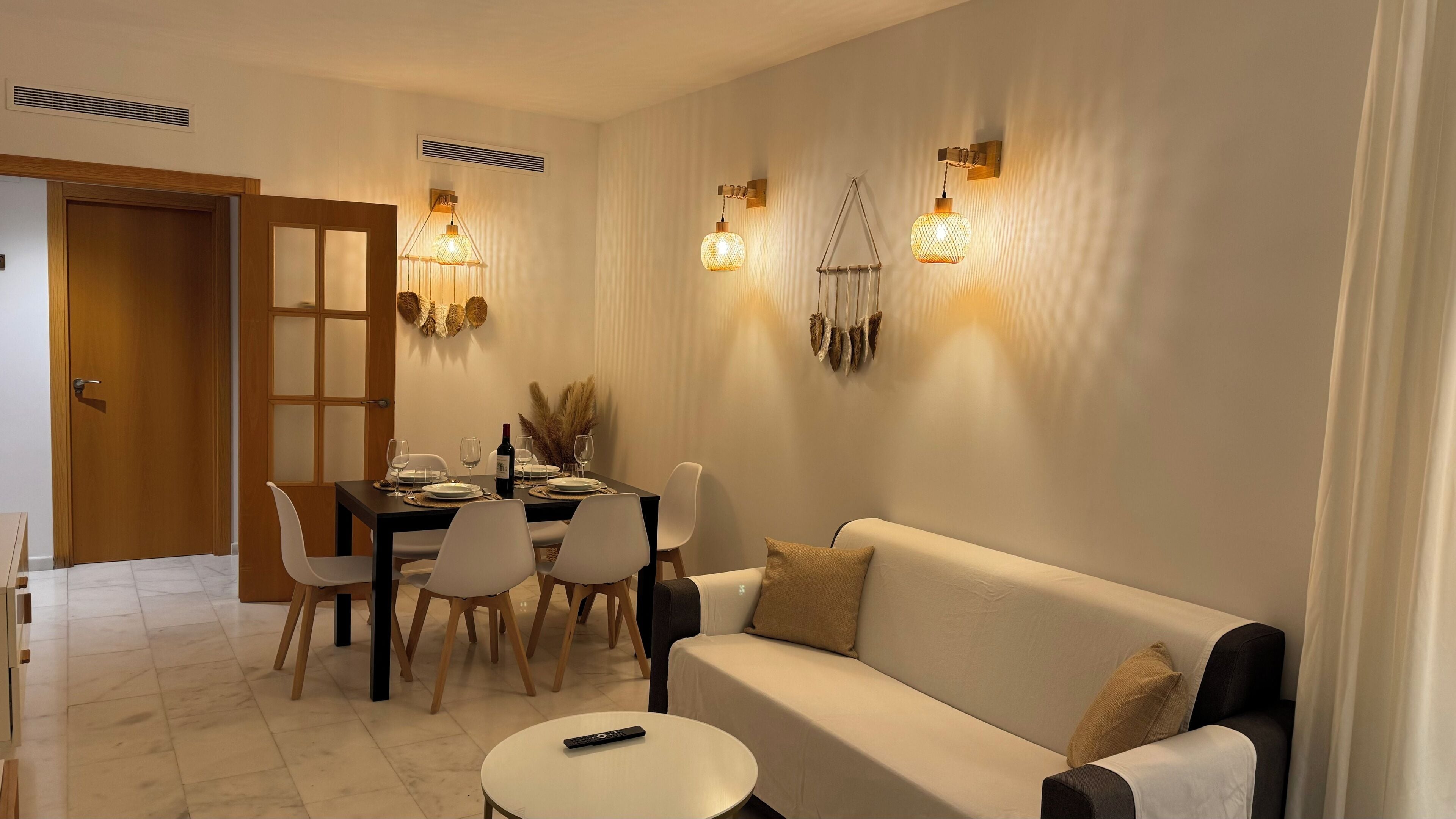A dining area with a table set for four, a sofa, and a remote control on a small table.
