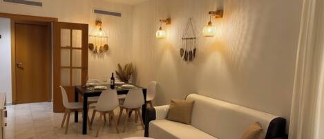 A dining area with a table set for four, a sofa, and a remote control on a small table.