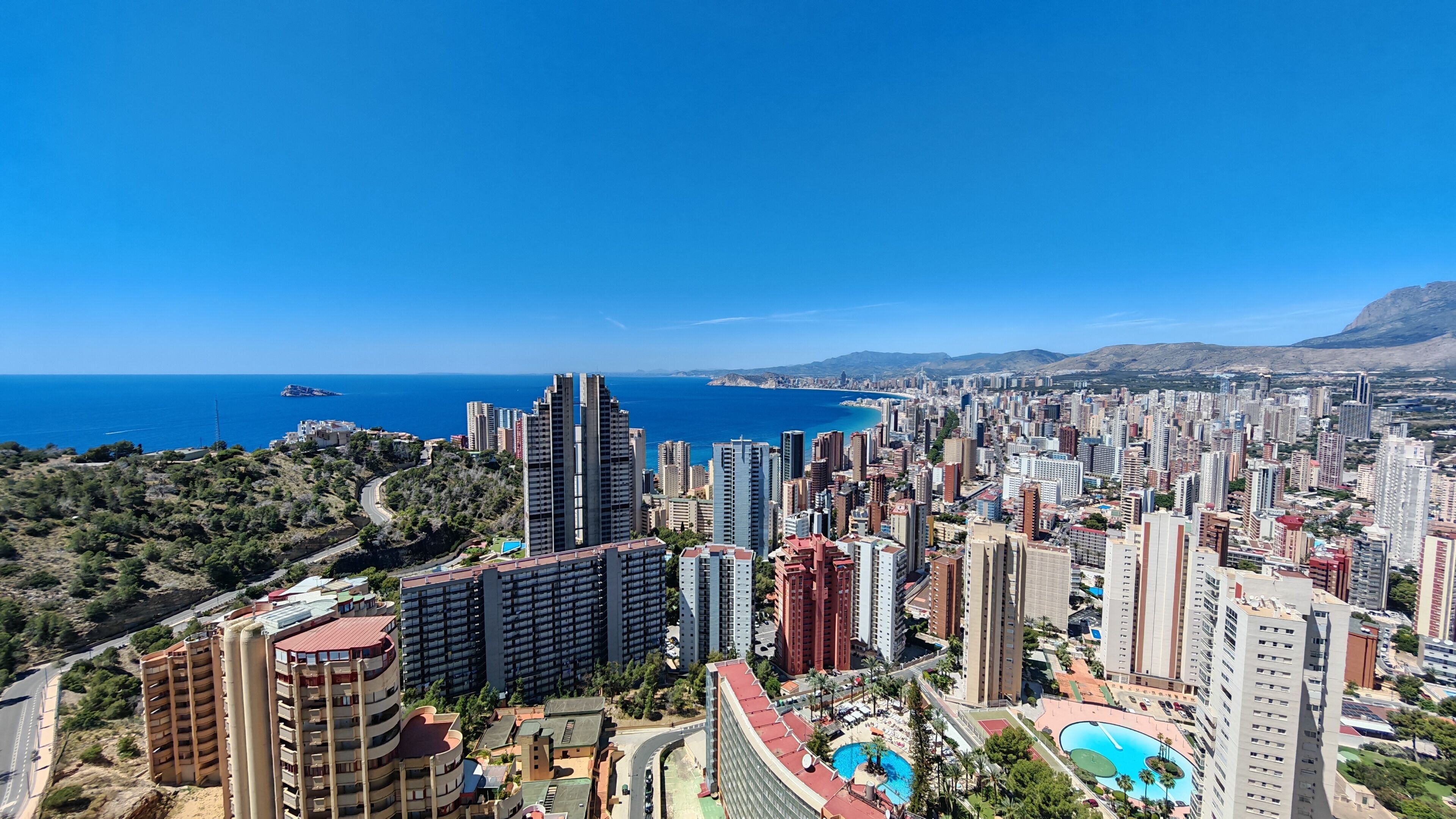 Un paisaje urbano con rascacielos, un cielo azul despejado y una costa al fondo.