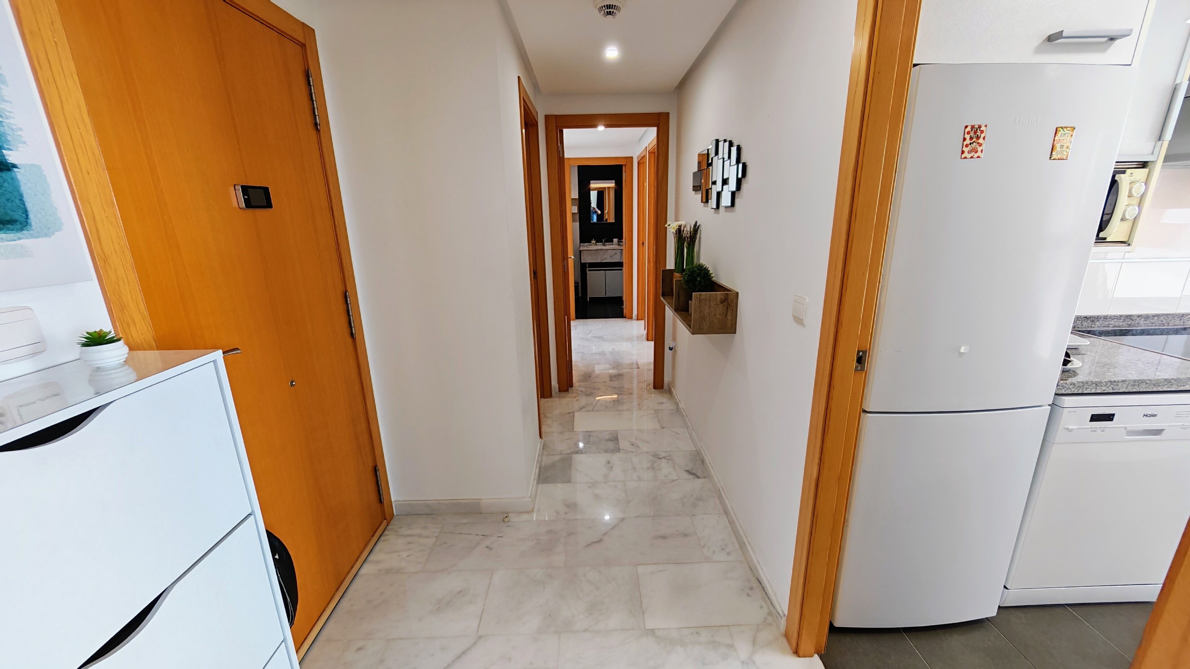 Un corridoio con frigorifero bianco, mobili in legno e pavimento in marmo.
