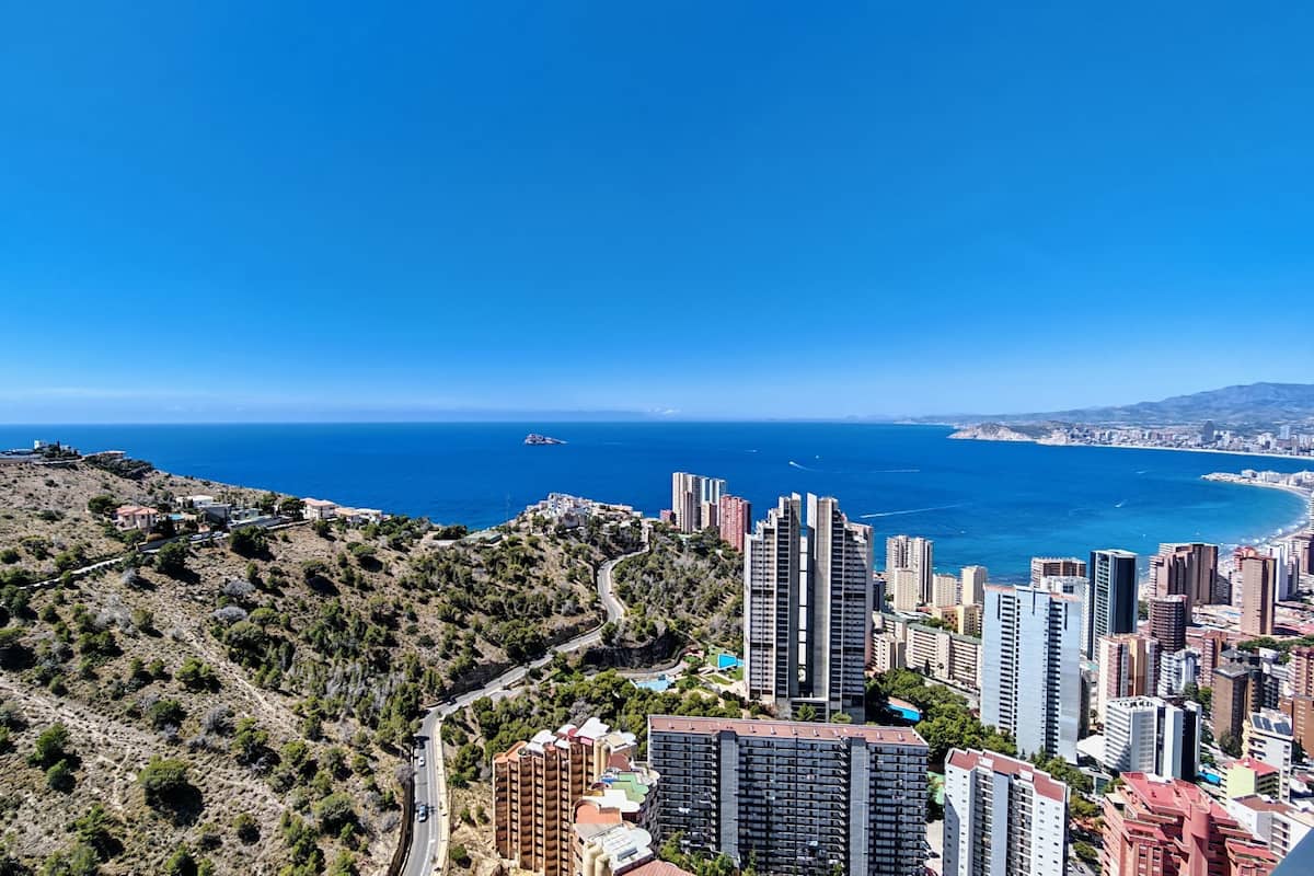 A coastal cityscape with high-rise buildings, a clear blue sky, and a view of the sea.