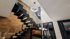 Un interior moderno con una escalera de caracol, barandilla de cristal y una lámpara de techo circular.