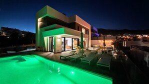 A modern multi-story building with a rooftop pool area, outdoor seating, and a well-lit entrance.