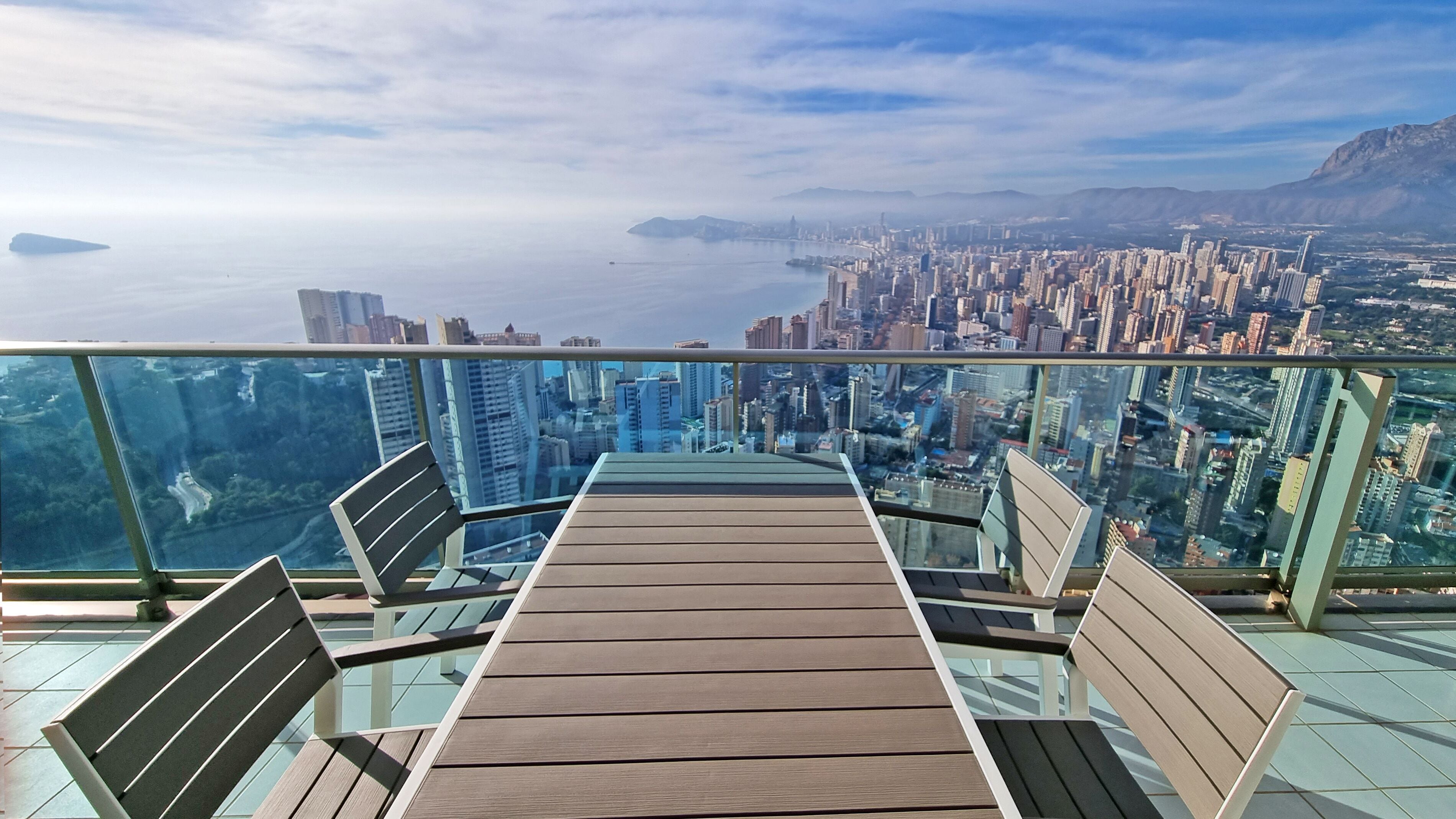 A balcony with a table and chairs, overlooking a cityscape and a body of water.