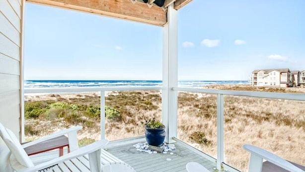 Une terrasse couverte offrant une vue sur la plage et l’océan, agrémentée d’une plante en pot et d’une chaise blanche.