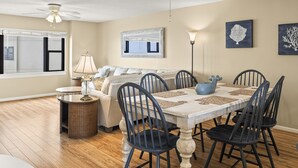 A dining area with a table set for four, surrounded by chairs, a ceiling fan, and a floor lamp.
