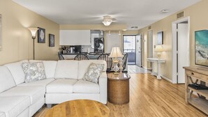 A living room with a white sofa, a wooden coffee table, and a dining area with chairs and a table.