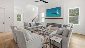 A spacious living room with a grey sectional sofa, a fireplace, and a large TV mounted on the wall. - Tailwinds & Tides | Heated Pool | Game Room | Rooftop Deck | Pet Friendly (Santa Rosa Beach)
