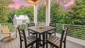 A covered outdoor patio with a table and chairs, surrounded by white railings and lush greenery. - Tailwinds & Tides | Heated Pool | Game Room | Rooftop Deck | Pet Friendly (Santa Rosa Beach)