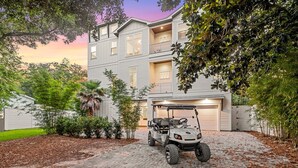A multi-story residential building with a garage, a golf cart, and a driveway with a brick surface. - Tailwinds & Tides | Heated Pool | Game Room | Rooftop Deck | Pet Friendly (Santa Rosa Beach)