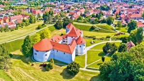 A large castle with multiple towers and a surrounding moat, surrounded by lush green fields and a dense residential area. - Romantic Haven With Hot Tub (Beretinec)