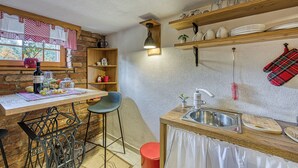 A kitchen with a wooden table, bar stools, a sink, and shelves with dishes and jars. - Romantic Haven With Hot Tub (Beretinec)