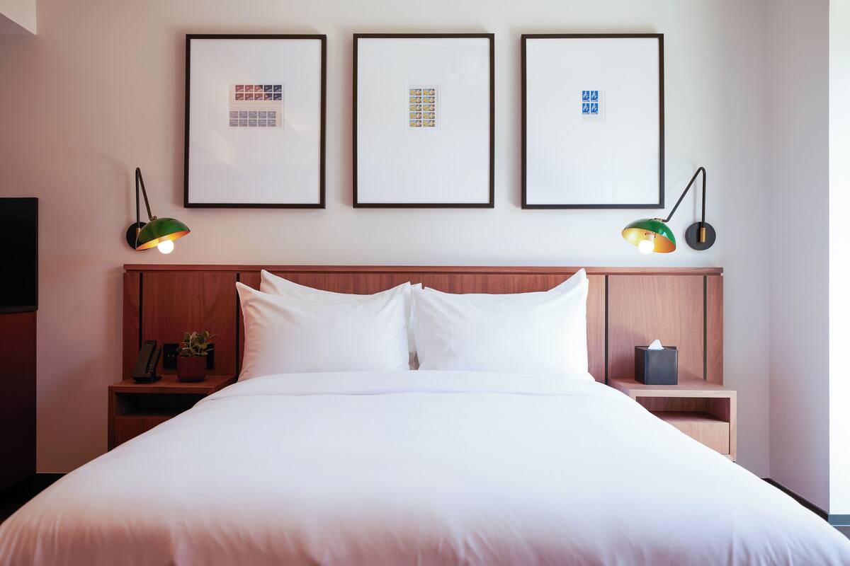 A neatly made bed with white linens, a wooden headboard, and two bedside tables with lamps.