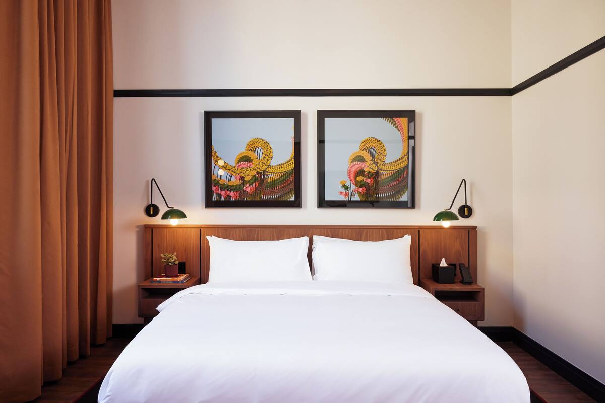 A hotel room with a large bed, two bedside tables with lamps, and two framed artworks on the wall.