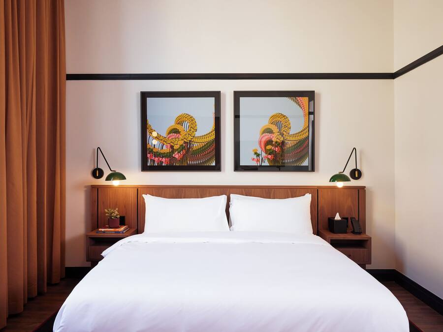 Une chambre d’hôtel avec un grand lit, deux tables de chevet avec des lampes et deux œuvres d’art encadrées accrochées au mur.