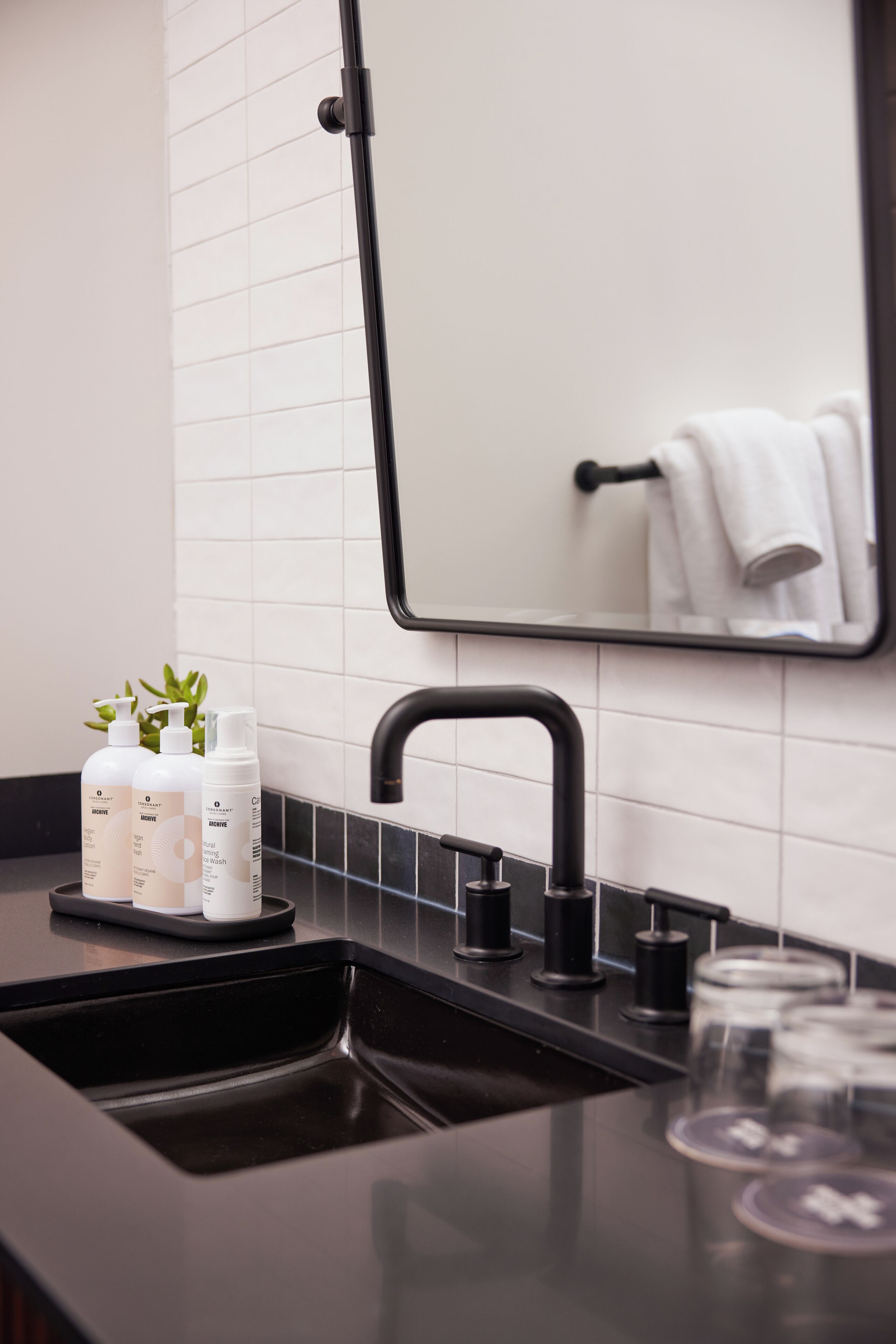 A modern bathroom with a black sink, a mirror, and three bottles of toiletries on the counter.