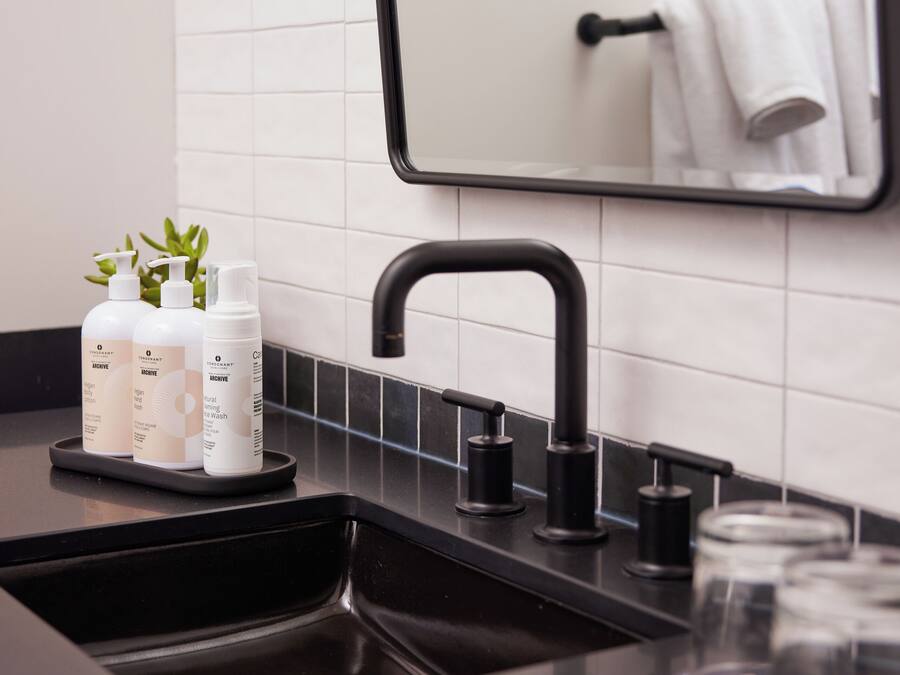 A modern bathroom with a black sink, a mirror, and three bottles of toiletries on the counter.