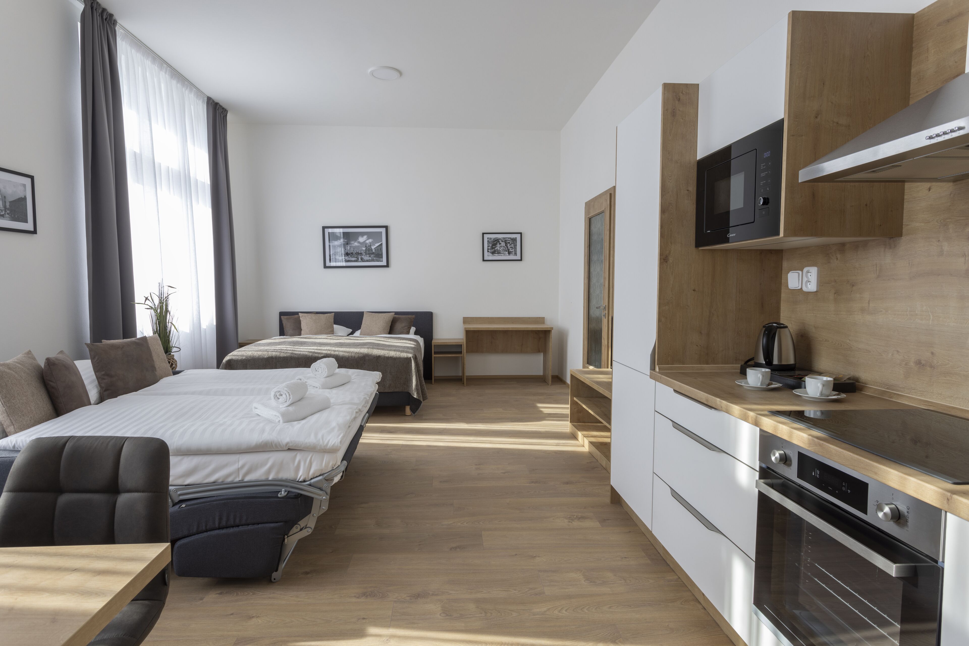A modern hotel room with a bed, bedside table, and a kitchenette with a microwave and oven.